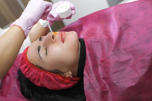 Cosmetologist making face care procedure. Specialist applying face mask to her client. Dermatology treatment. Facial peeling.