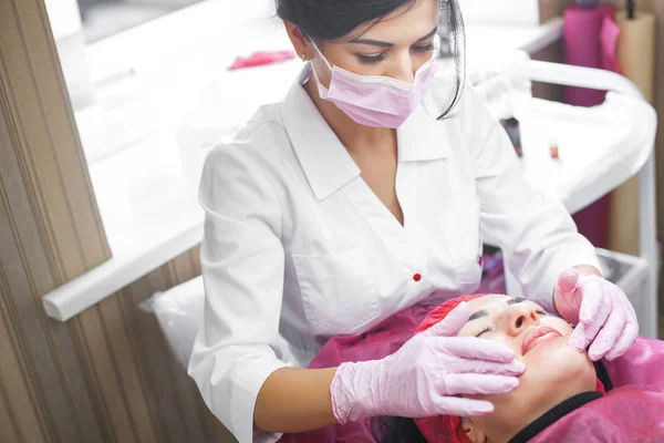 Cosmetologist making face care procedure. Specialist applying face mask to her client. Dermatology treatment. Facial peeling.