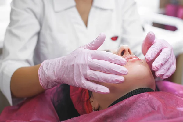 Cosmetologist making a face massage to her patient and a face mask. Anti-ageing and smoothing procedure in a beauty salon. Doctor in a cosmetological clinic making a treatment of skin care