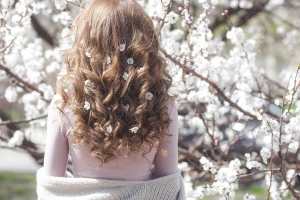 Long haired woman outdoors on spring background. Unrecognizable lady with flowers in hair. Curly haired female.