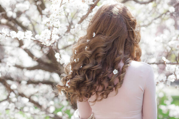 Длинноволосая женщина на весеннем фоне. Неузнаваемая женщина с цветами в волосах. Кудрявая самка
.