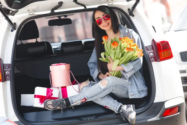 新鮮な花の花束を保持するスプリングの若い美しい女性の肖像画 屋外のチューリップを持つ少女 白い車の近くに立ってチューリップと陽気な女性 — ストック写真