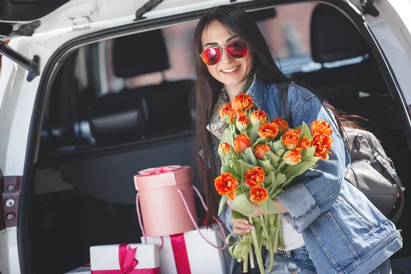 車の中で若い魅力的な女性は ボックス ギフト 花をプレゼントします 春にチューリップの花束を持つ美しい女性 自動車の女性 — ストック写真