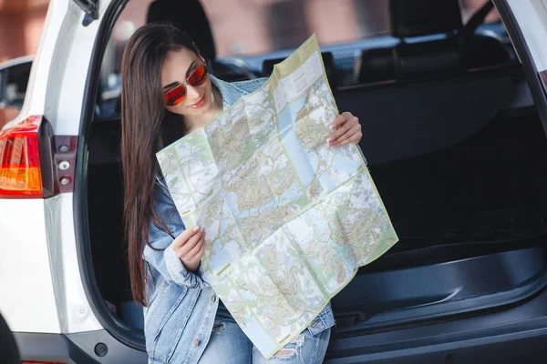 Young woman holding map of the city. Attractive girl on the car travel. Driver with map.