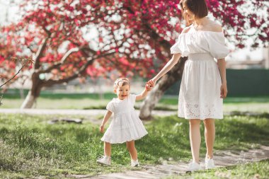 Genç ve sevgi dolu bir anne bahar arka planında küçük bebeğiyle yürüyor. Tatlı bir çocuk ve annesi dışarıda. Ailesi parkta..