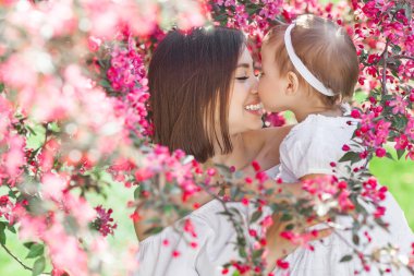 Genç anne ve küçük kızının yakın çekim resmi. Güzel bir aile dışarıda. Anne onun küçük sevimli çocuk ile oynuyor.