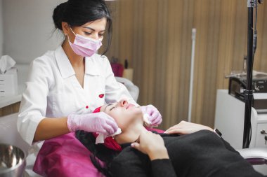 Kozmetolojist yüz germe işlemi yapıyor. Dermatolojit yüz maskesi uyguluyor. Klinikte güzellik tedavisi.