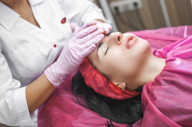 Kozmetolojist yüz germe işlemi yapıyor. Dermatolojit yüz maskesi uyguluyor. Klinikte güzellik tedavisi.