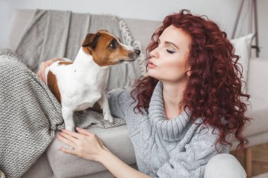 Genç bir kadın evcil hayvanıyla oynuyor. Dişi ve köpeği içeride. Ev sahibi ve evcil hayvanı eğleniyor. Jack Russel terrier 'i komutları yerine getirmek için eğiten kadın.