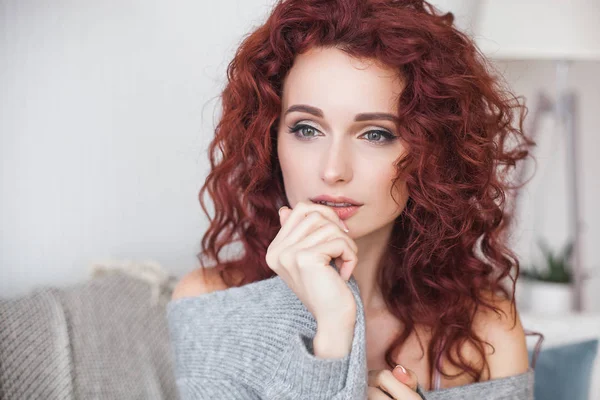 Very attractive young woman indoors. Portrait of curly haired female. Redhaired beautiful woman at home.