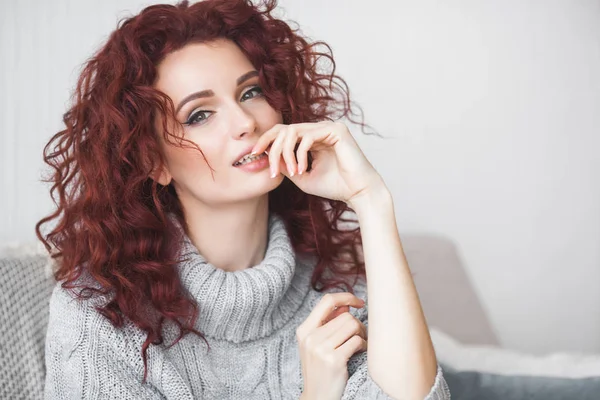 Very attractive young woman indoors. Portrait of curly haired female. Redhaired beautiful woman at home.
