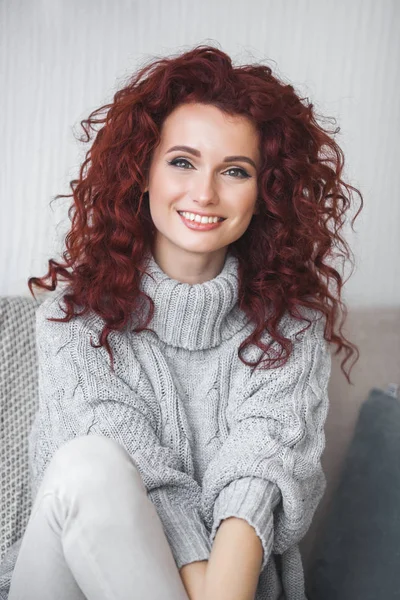 Very attractive young woman indoors. Portrait of curly haired female. Redhaired beautiful woman at home.