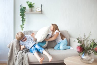 Küçük çocuklar içeride eğleniyor. Kanepede oynayan çocuklar. Yastık savaşı. Erkek ve kız kardeş evde karışıklık yapma.