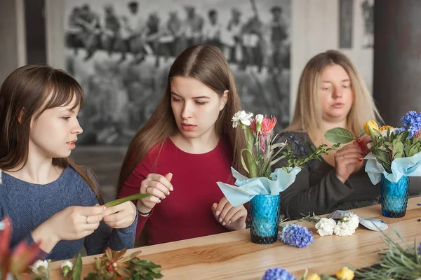 Women on the master-class on floristics. Young ladies making floral composition. Group of females with flowers indoor at the loft background. Decoration process.