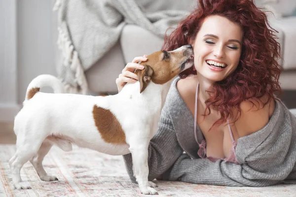 Young woman playing with her pet. Female and her dog indoor. An owner and his pet at home having fun. Woman training jack russel terrier to execute commands.