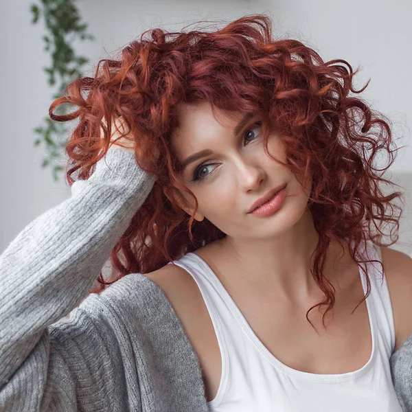 Very attractive young woman indoors. Portrait of curly haired female. Redhaired beautiful woman at home.