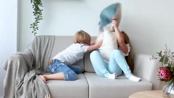 屋内で楽しむ小さな子供たち ソファで遊ぶ子供たち 枕の戦い 家で混乱を作る兄弟姉妹 — ストック動画