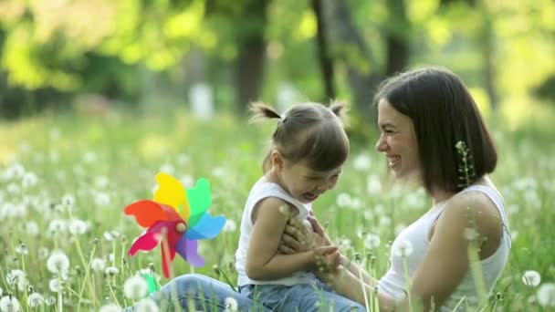 若い幸せな母親と彼女の小さな娘はタンポポと草原で遊んでいます 屋外で幸せな家族 女性と彼女の子供は夏の背景に一緒に — ストック動画