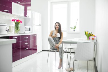 Sabahın köründe mutfakta kahve içen genç ve güzel bir kadın. Taze bir sabah. Parlak bir içki. İş ücretleri. Uyanık bayan..