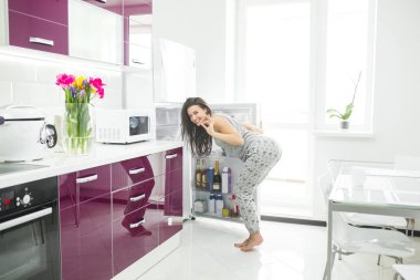 Young woman on the kitchen opening a fridge. Female indoors in the morning. Cheat meal. glutton girl. clipart