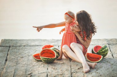 Genç güzel anne ve onun bebek kız gün batımında sahilde oturan portresi. Dışarıda çocuğuna sarılan kadın. Genç anne ve karpuzile sahilde onun küçük sevimli kızı.