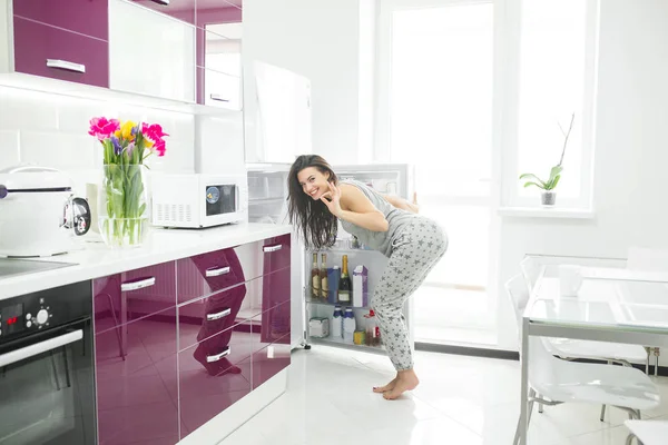 Young woman on the kitchen opening a fridge. Female indoors in the morning. Cheat meal. glutton girl.