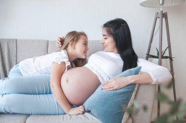 Genç hamile anne ve küçük kızı içeride. Çocuk ve annesi yeni doğmuş bir bebeği bekliyorlar. Mutlu aile bekliyor..
