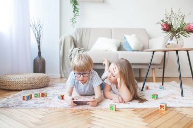 Akıllı telefon oynayan küçük sevimli çocuklar. Evde video oyunları oynayan erkek ve kız kardeş.