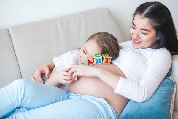 Young pregnant mother and her little daughter indoors. Child and her mom waiting for a little new born baby. Happy family expecting.