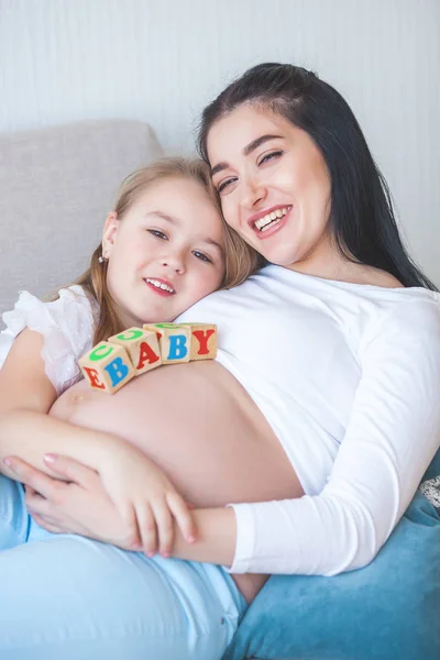 Young pregnant mother and her little daughter indoors. Child and her mom waiting for a little new born baby. Happy family expecting.