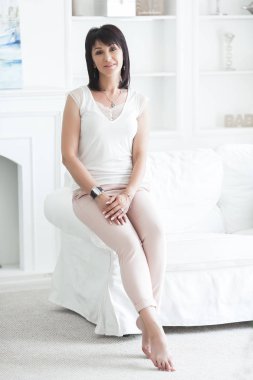 Kapalı kanepede oturan çekici yetişkin kadın. Evde güzel orta yaş kadın. 35-40 yaş kadın portresi.