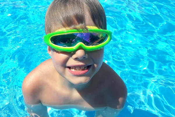 Funky kid in the pool. Funny child playing in the swimming pool. Summer games. Cute boy playing in the water on summertime wearing goggles.