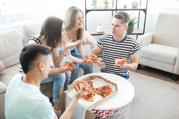 Young people eating pizza. Group of friends having lunch indoors. Funny friends together.