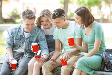 Neşeli arkadaşlar cep telefonunda yazı yazıyor. Akıllı telefona bakan genç insanlar. Dışarıda cep telefonları ve kahveleri olan bir grup arkadaş..