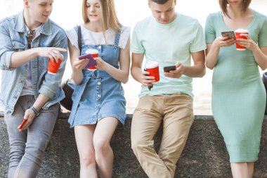Neşeli arkadaşlar cep telefonunda yazı yazıyor. Akıllı telefona bakan genç insanlar. Dışarıda cep telefonları ve kahveleri olan bir grup arkadaş..