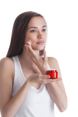 Yüz kremi uygulayan genç çekici kadının closeup portresi. Kadın nemlendirici yüz kremi ile bir kavanoz tutarak.