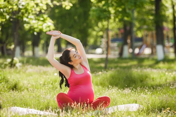 Parkta açık havada yoga egzersizleri yapan çekici genç hamile kadın. Sağlıklı ve aktif bir yaşam tarzına sahip kadın beklentisi.