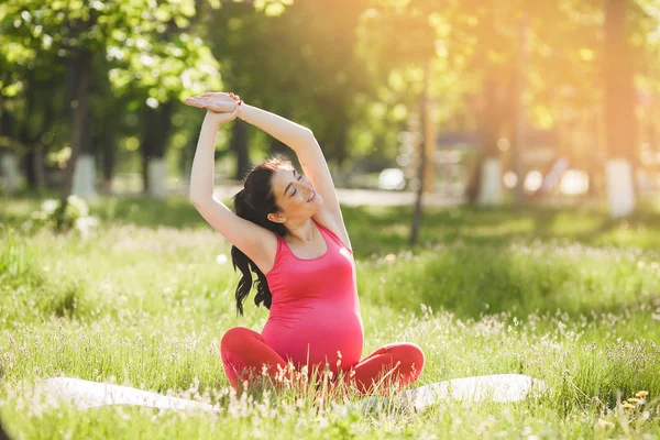 Parkta açık havada yoga egzersizleri yapan çekici genç hamile kadın. Sağlıklı ve aktif bir yaşam tarzına sahip kadın beklentisi.