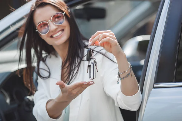 Young attractive woman just bought a new car. female holding keys from new automobile.