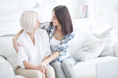 Olgun anne ve yetişkin kızı birlikte. İçerideki kadınlar portresi. Orta yaş kadın ve kızı evde kanepede oturan.