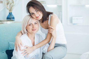 Olgun anne ve yetişkin kızı birlikte. İçerideki kadınlar portresi. Orta yaş kadın ve kızı evde kanepede oturan.