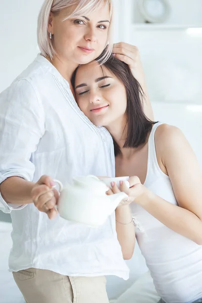 two women talking. Mother and daughter indoors together.Ladies drinking tea. Two females at home. Mature mother and her adult daughter embracing.