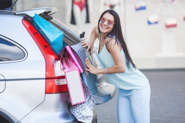 Çekici genç kız bir arabaya perakende bir sürü koymak için çalışıyor. Alışveriş çantalarını bavullara koyan kadın. Alışveriş çantalarını bagaja sokarken genç kadın.