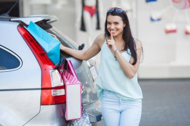 Çekici genç kız bir arabaya perakende bir sürü koymak için çalışıyor. Alışveriş çantalarını bavullara koyan kadın. Alışveriş çantalarını bagaja sokarken genç kadın.