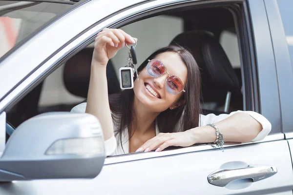 Young attractive woman just bought a new car. female holding keys from new automobile.