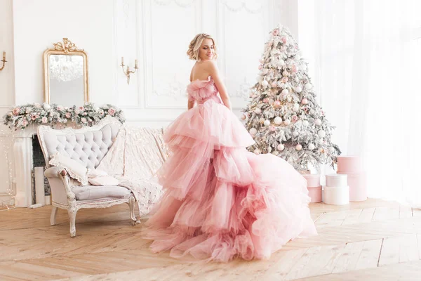 年轻美丽的金发女人在圣诞背景全高 迷人的女士在粉红色华丽的礼服 — 图库照片