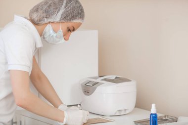 Manikürcü otoklav veya fırında onu araçları sterilize. Salonda usta dezenfeksiyon için onun aletleri hazırlanıyor.