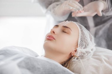 Usta müşterisi için kozmetik bir işlem yapıyor. Cilt bakımı. Kadın yüz bakımı prosedürü uyguluyor.