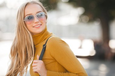 Çekici, genç, sarışın kadın portresi. Sonbahar güneşinin arka planında açık havada bir kadın. Sonbaharda neşeli bir kadın portresi..