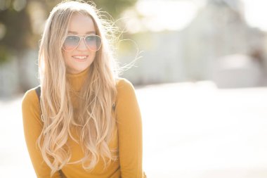 Çekici, genç, sarışın kadın portresi. Sonbahar güneşinin arka planında açık havada bir kadın. Sonbaharda neşeli bir kadın portresi..